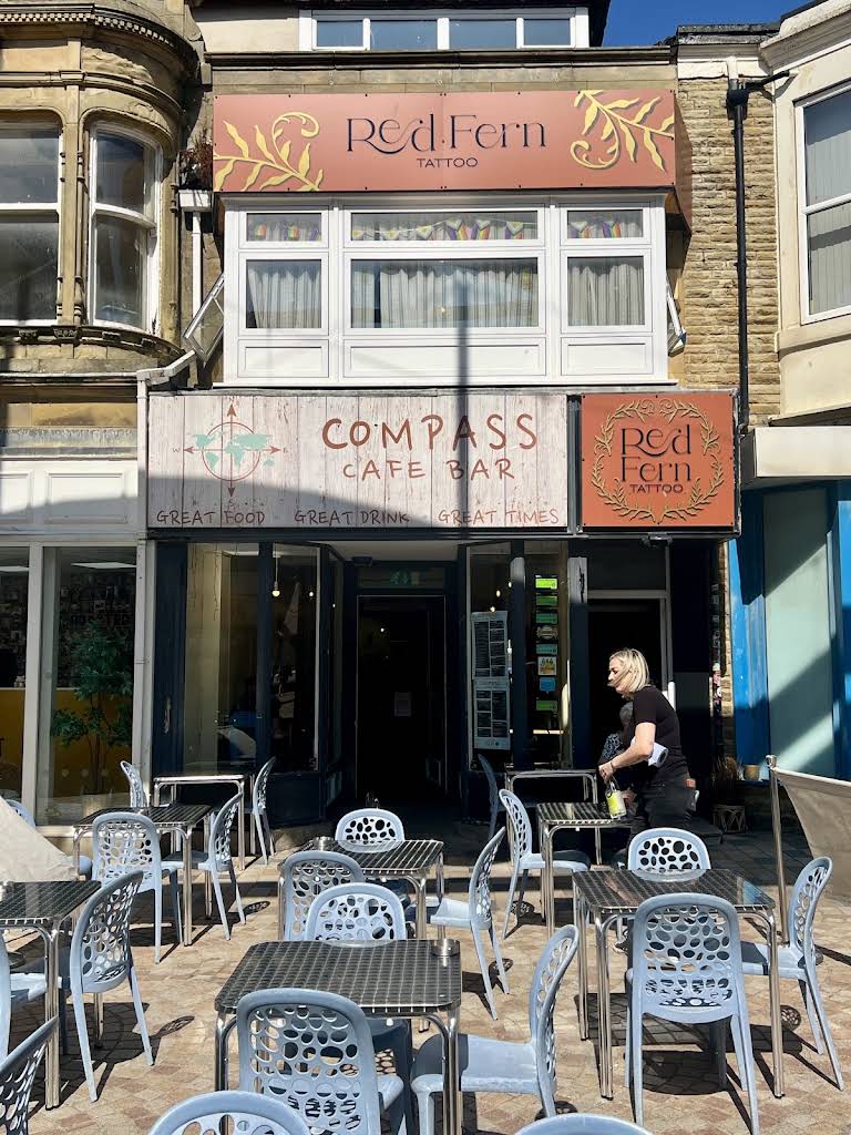 The complete Compass Café Bar timber sign, pale turquoise compass motif, doors, pavement and outdoor chairs on Birley Street