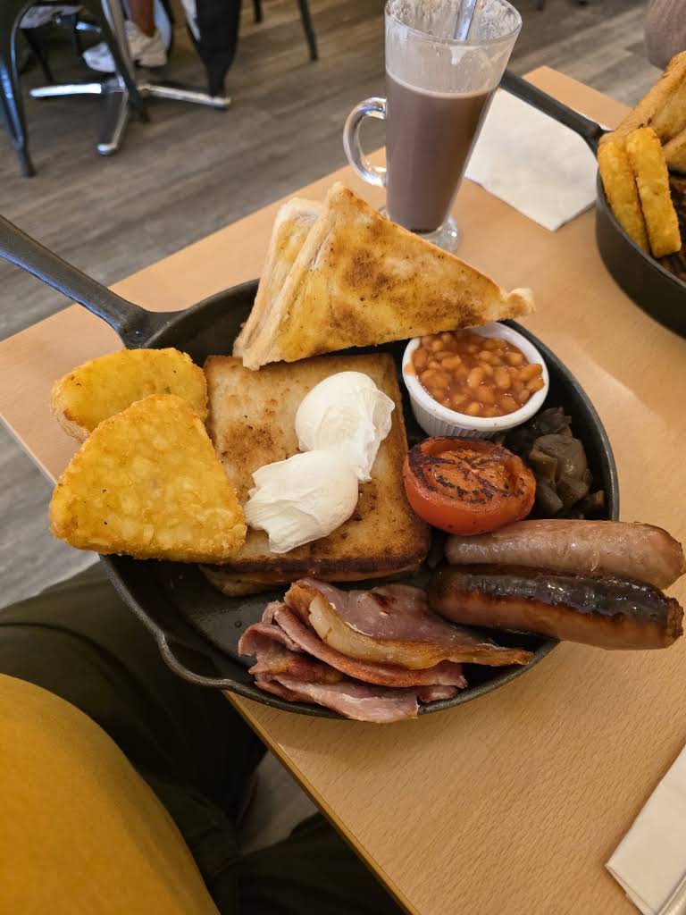 Breakfast served in a black pan on a wooden table, with a glass drink alongside